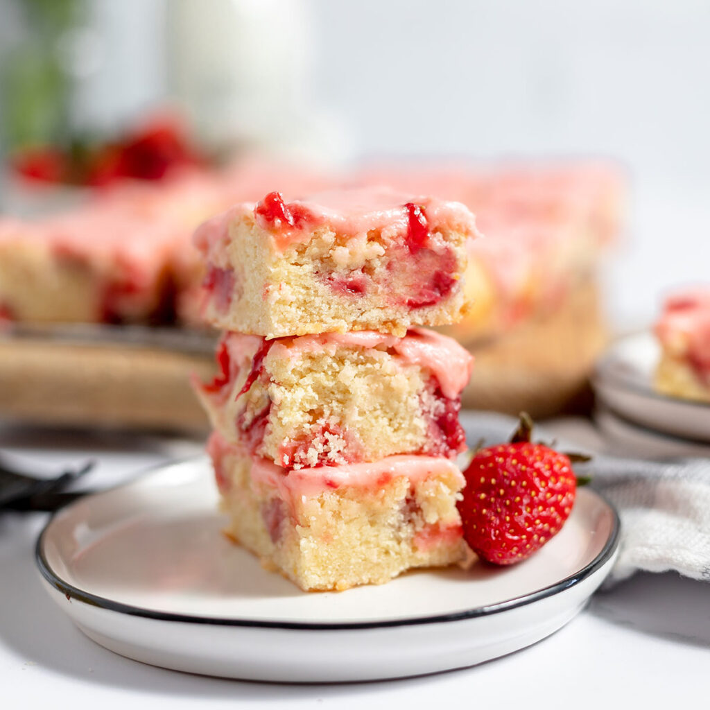 Three Strawberry Lemon Blondies stacked on a white plate.