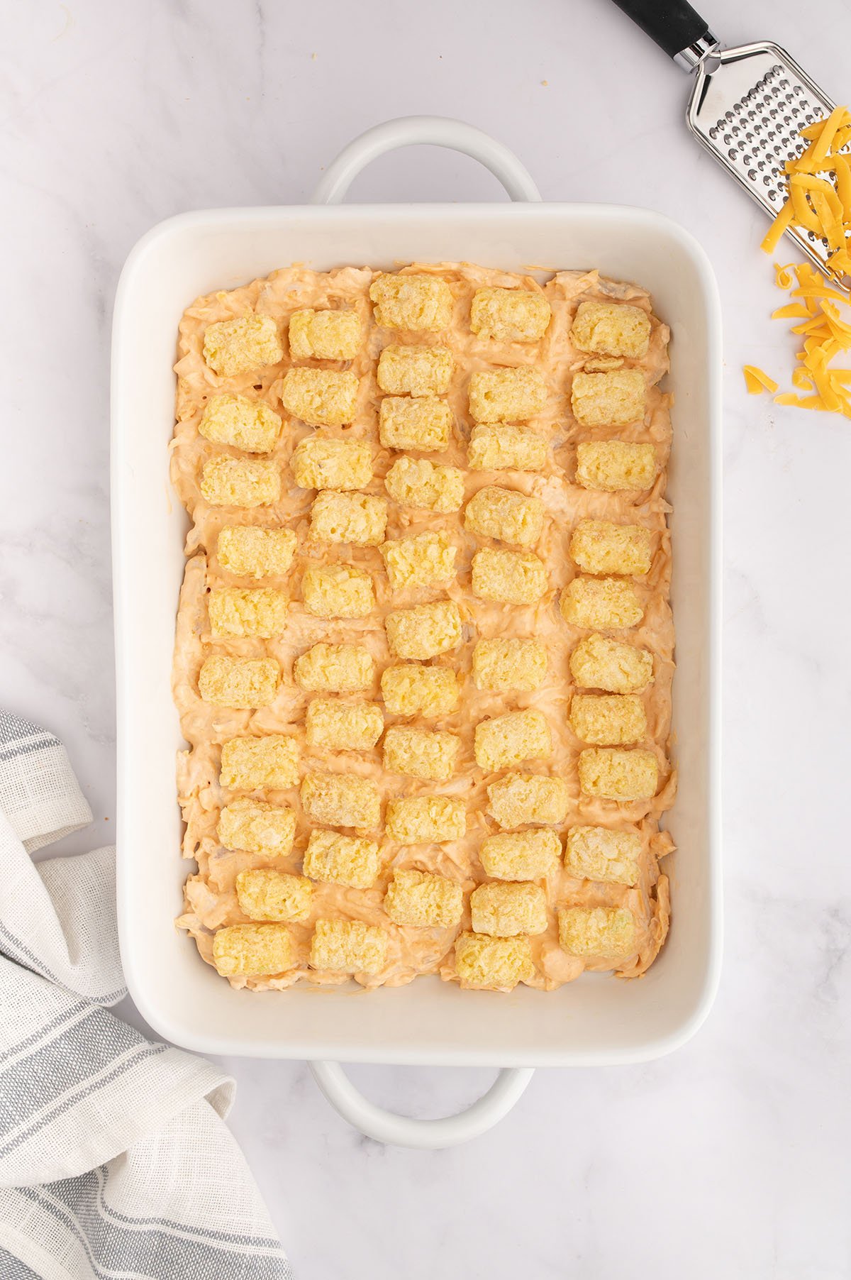 Tater tots placed over the buffalo chicken filling in the baking dish.