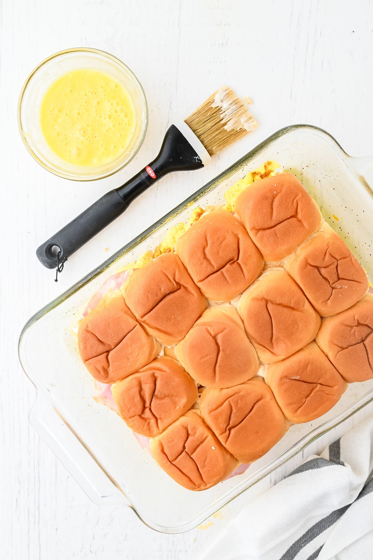 The top half of Hawaiian rolls is placed over ham, cheese, and egg in a baking dish.