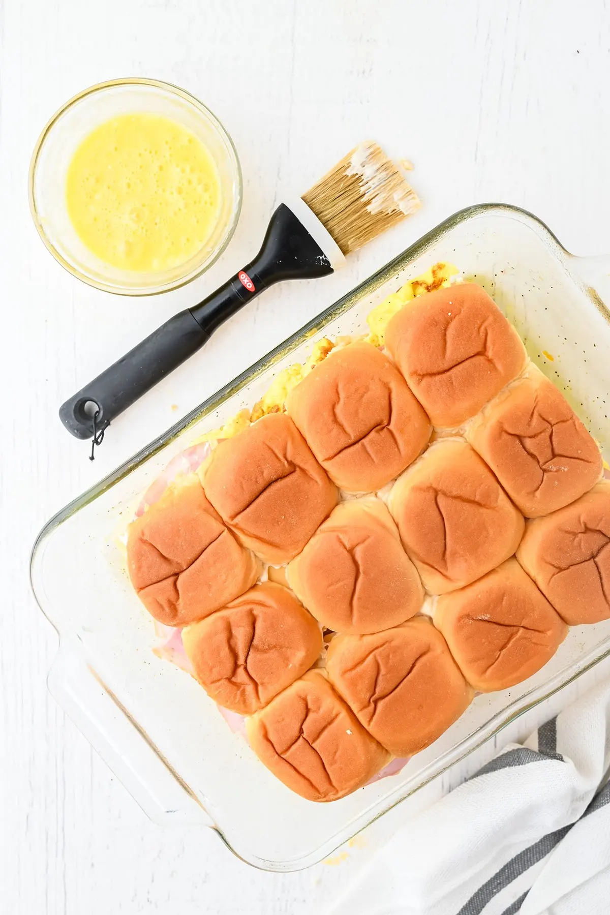 The top half of Hawaiian rolls is placed over ham, cheese, and egg in a baking dish.