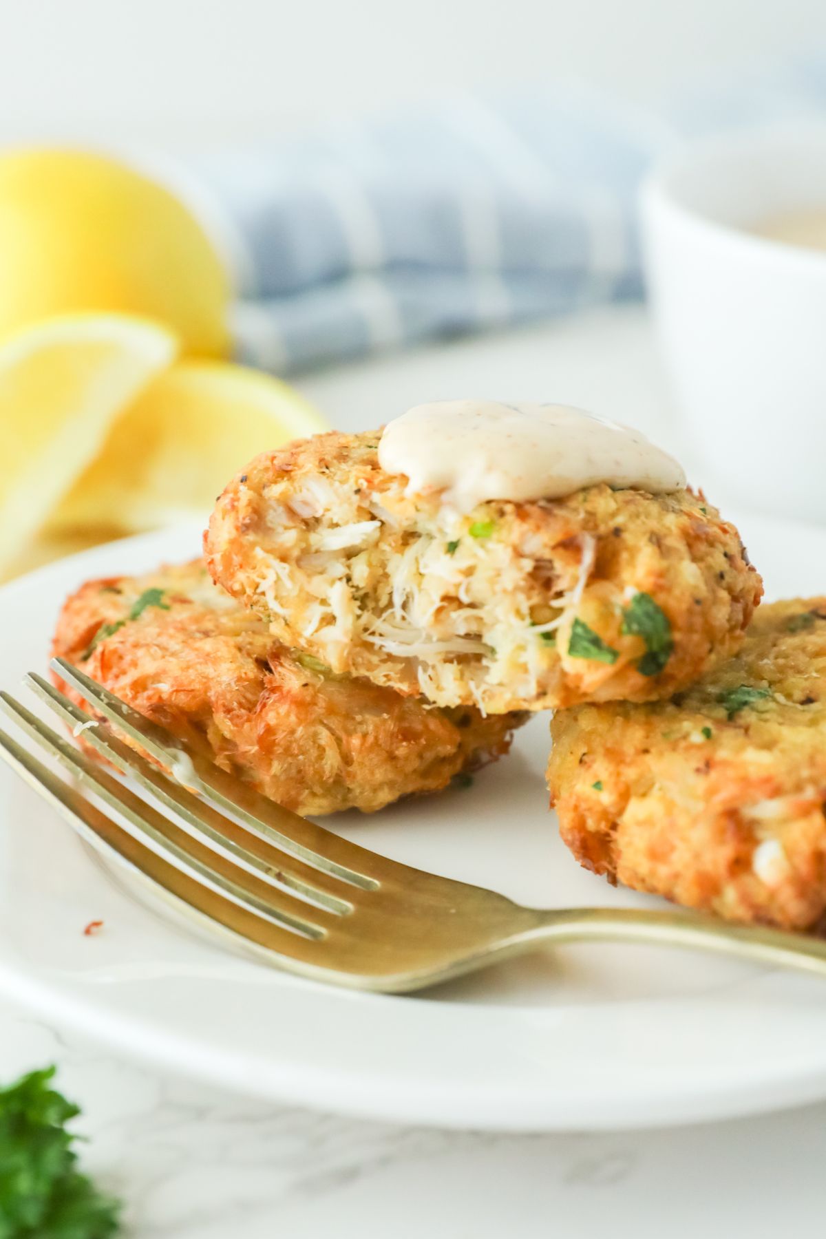 Three crab cakes on a white plate with a bite out of one.