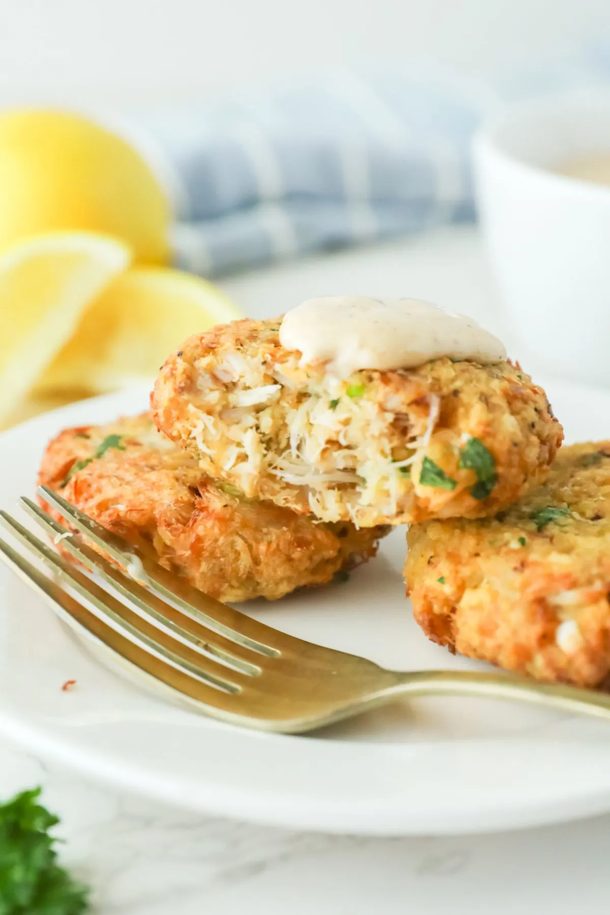 Three crab cakes on a white plate with a bite out of one.