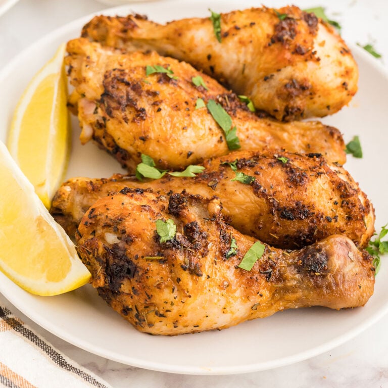 Four chicken legs on a white plate with slices of lemon.