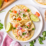 Two Cod Fish Tacos on a plate with lime slices.