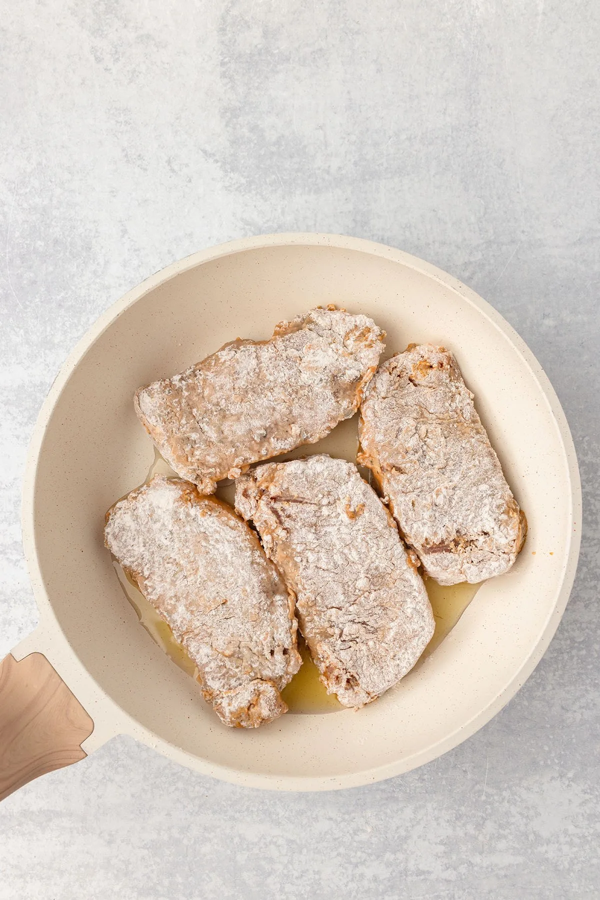 Flour coated pork chops placed in skillet.
