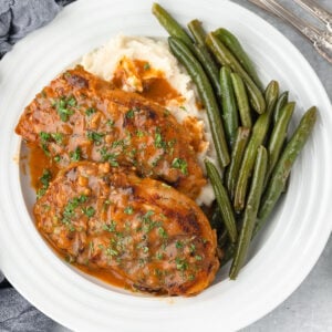 Two Honey Mustard Pork Chops served on a plate with green beans and mashed potatoes.