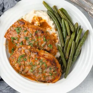 Two Honey Mustard Pork Chops served on a plate with green beans and mashed potatoes.