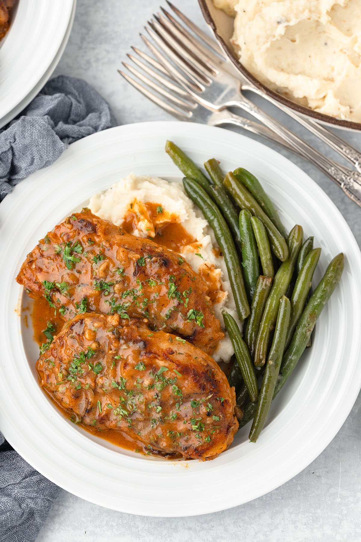 Two Honey Mustard Pork Chops on a white plate with green beans and mashed potatoes.