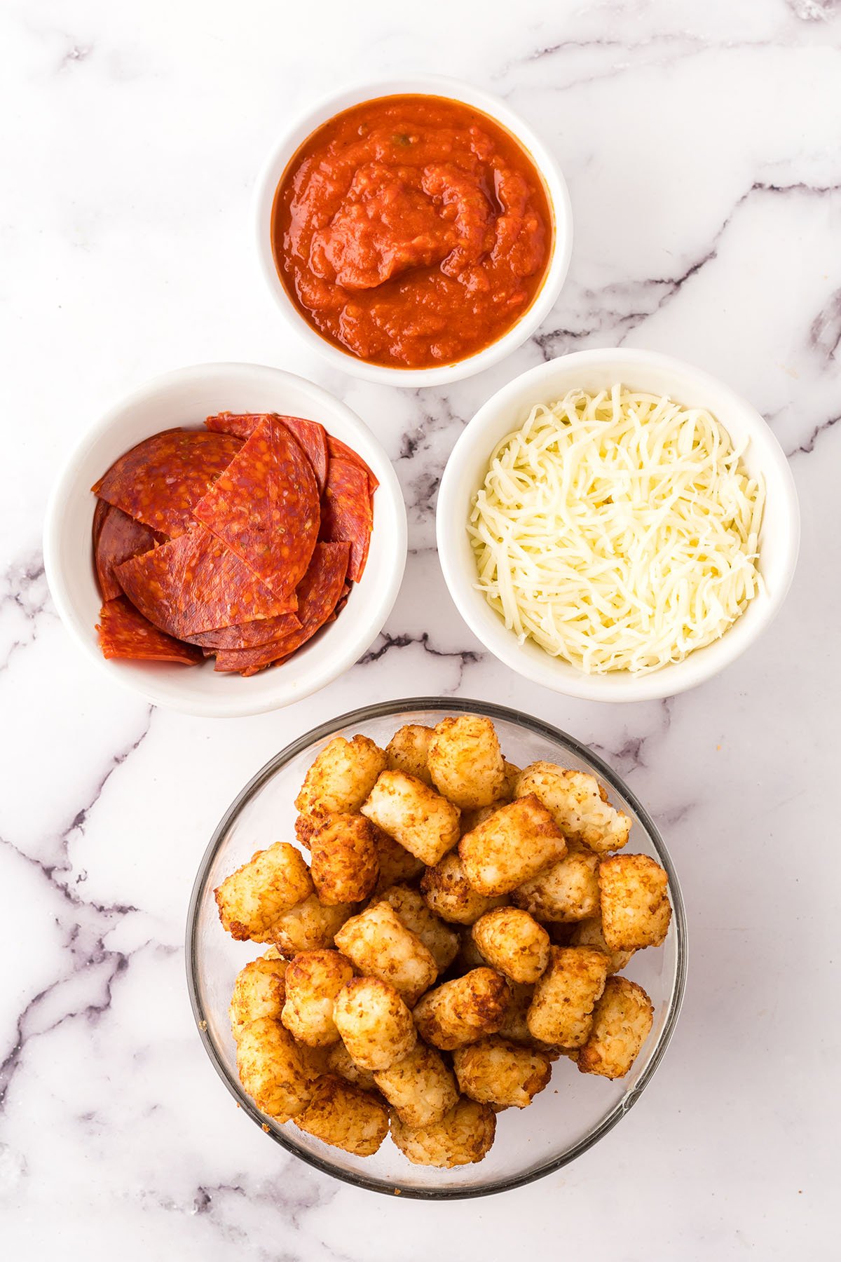 Ingredients to make Pepperoni Pizza Totchos set out on the counter in bowls.