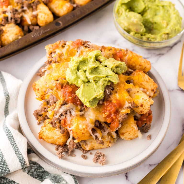 A serving of Mexican Totchos topped with guacamole on a plate.