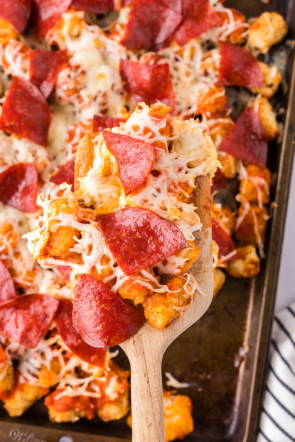 Pizza Totchos on a baking sheet with a serving on a large wooden spoon.
