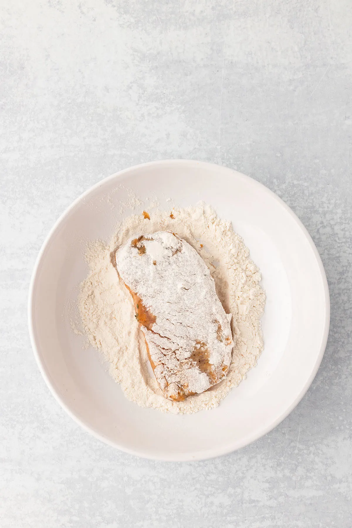 Pork chops are coated in flour in a bowl.