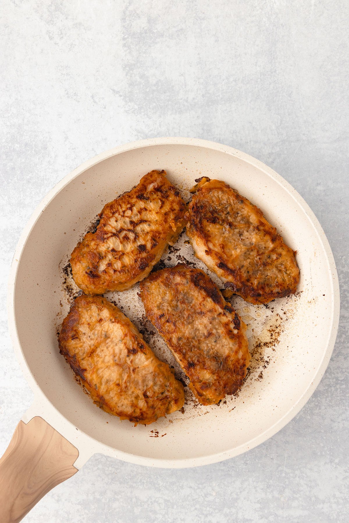Pork chops cooked in oil in a skillet.