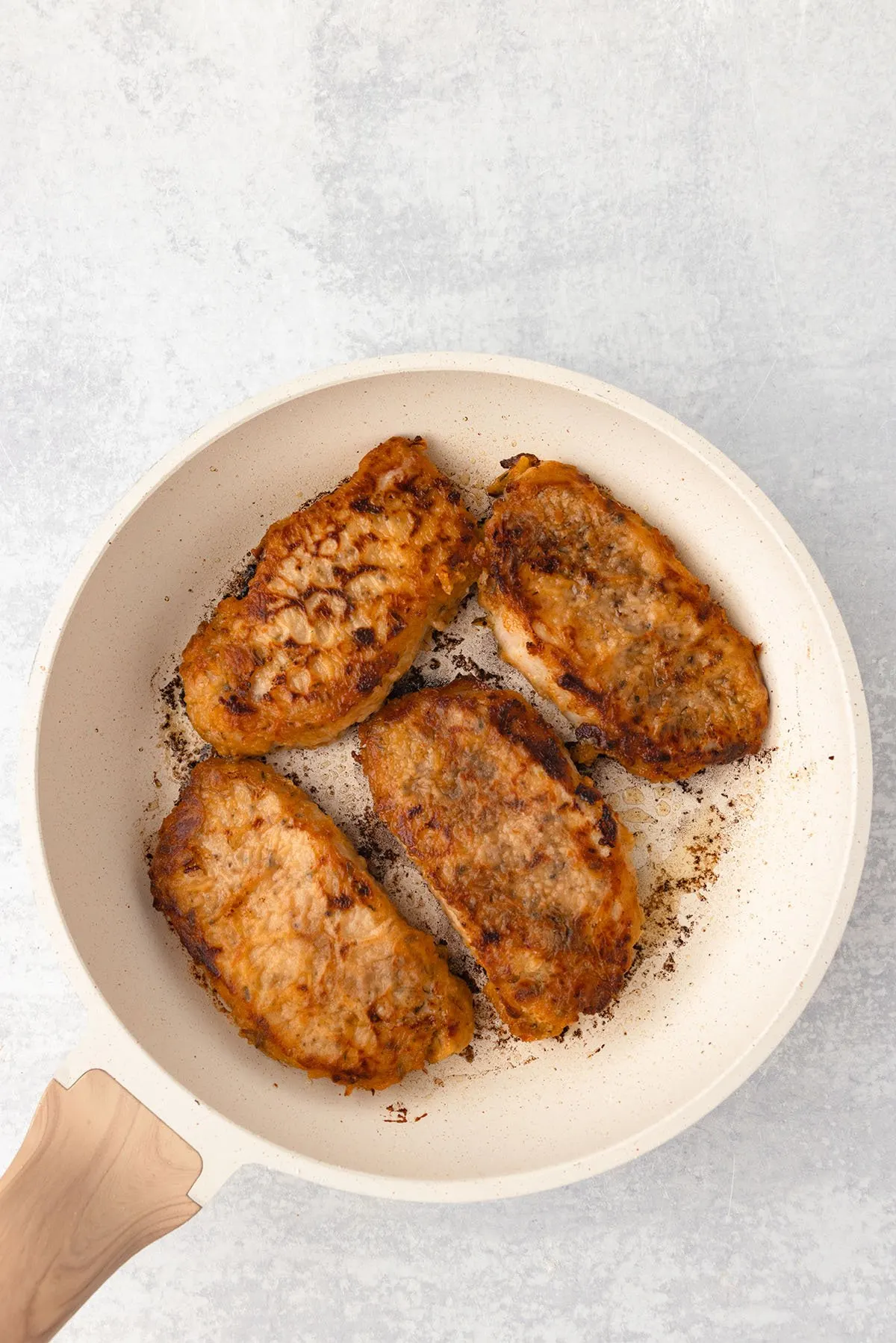 Pork chops cooked in oil in a skillet.