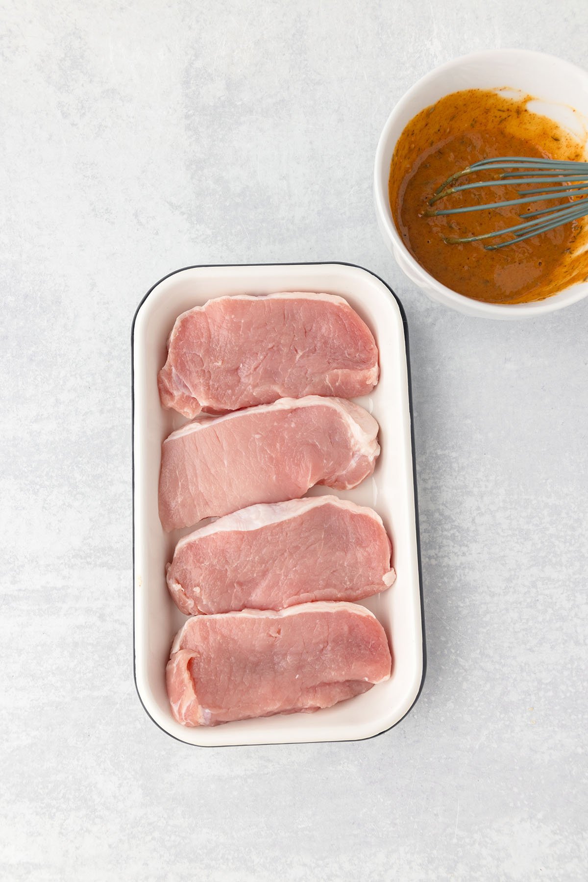 Pork chops are in shallow container in a single layer.