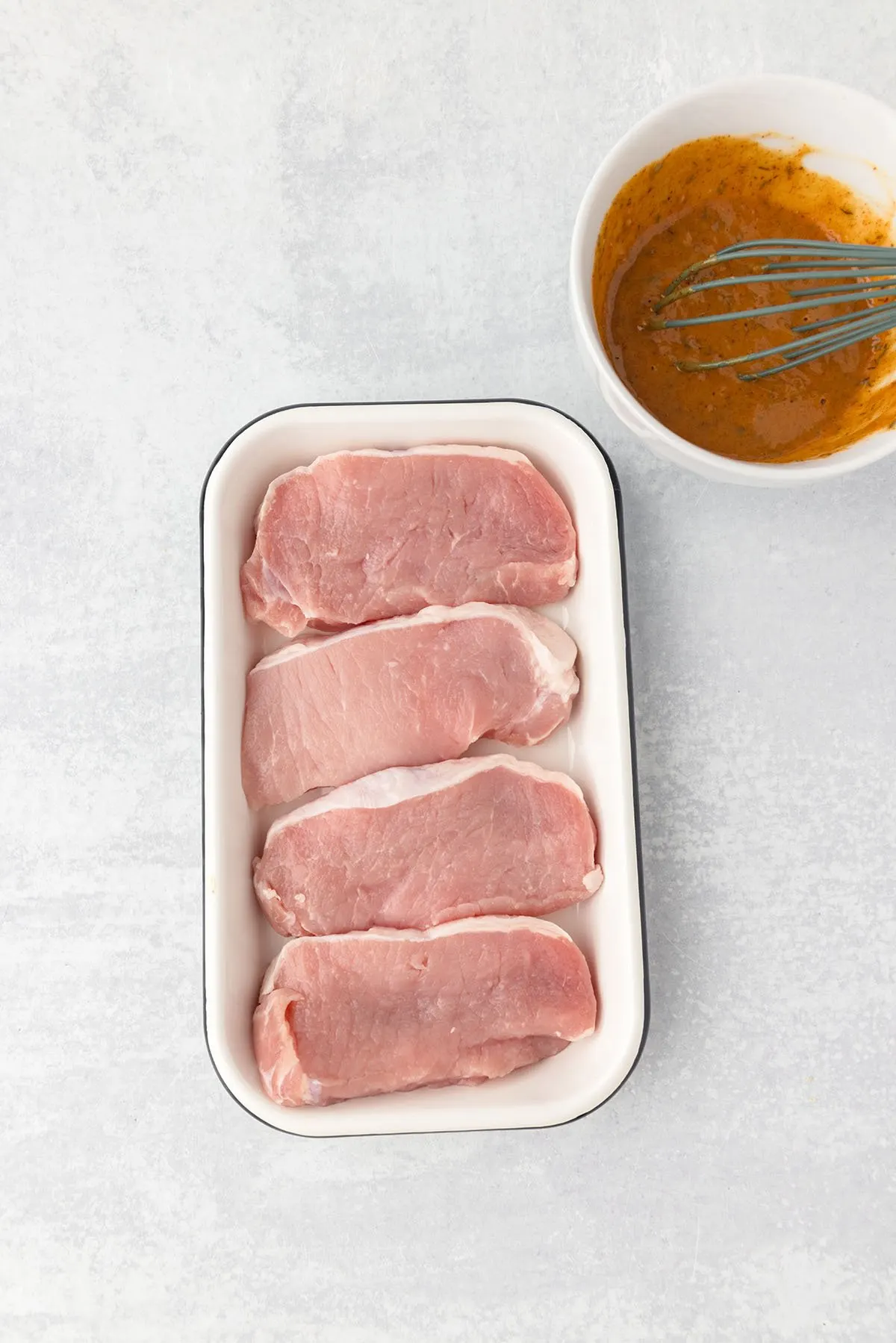 Pork chops are in shallow container in a single layer.