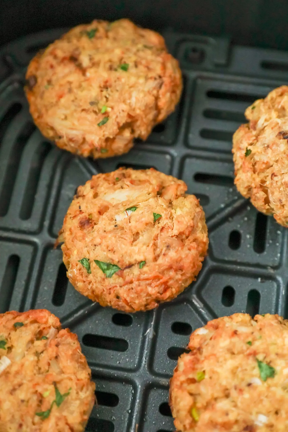 Air-fried crab cakes in an air fryer basket ready to serve.