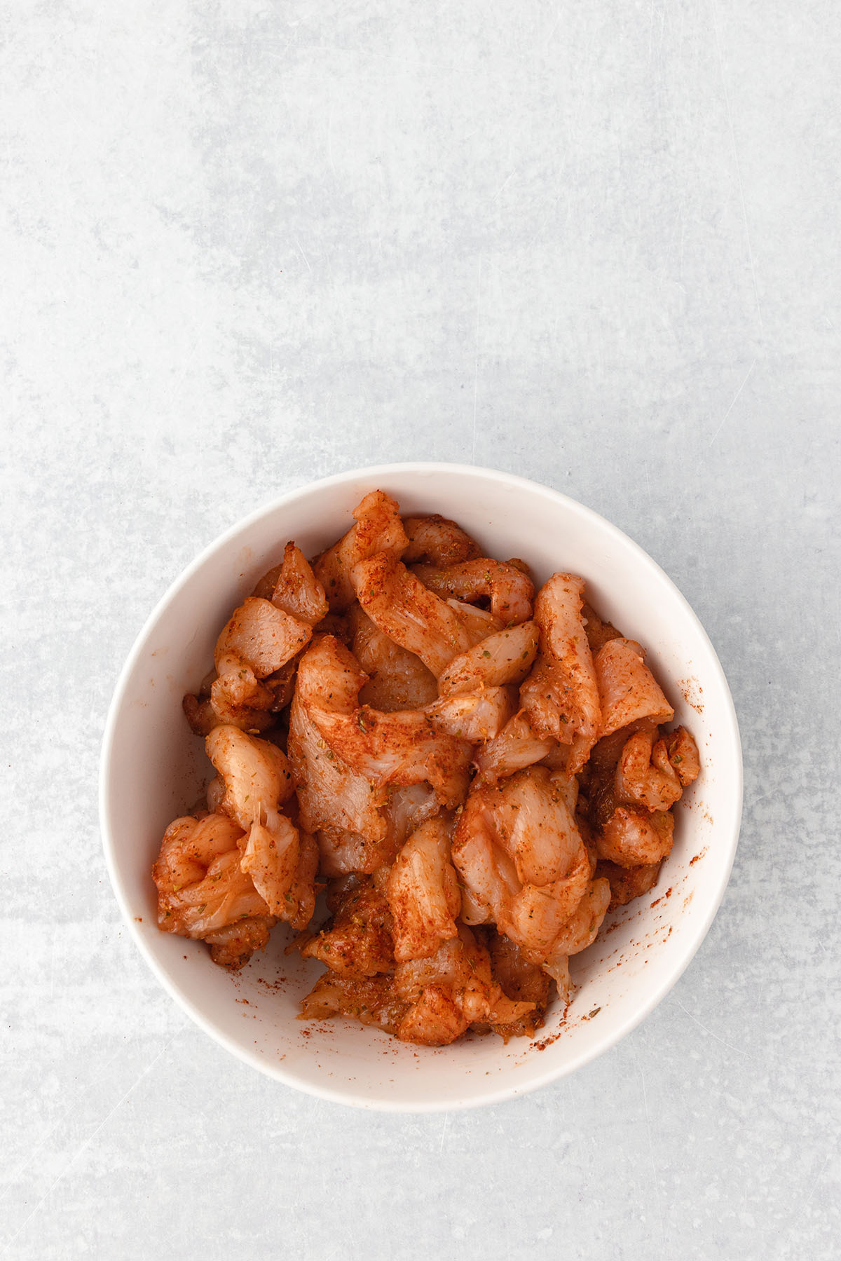 Thinly sliced chicken coated with seasonings in a large bowl.