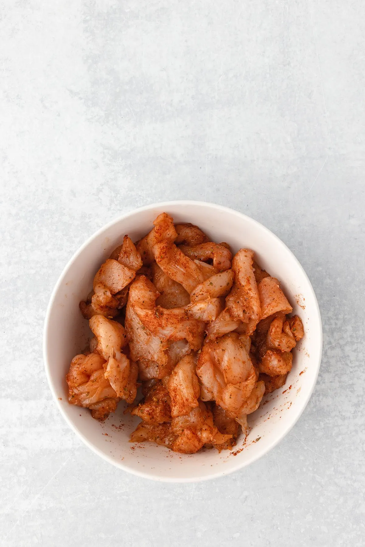 Thinly sliced chicken coated with seasonings in a large bowl.