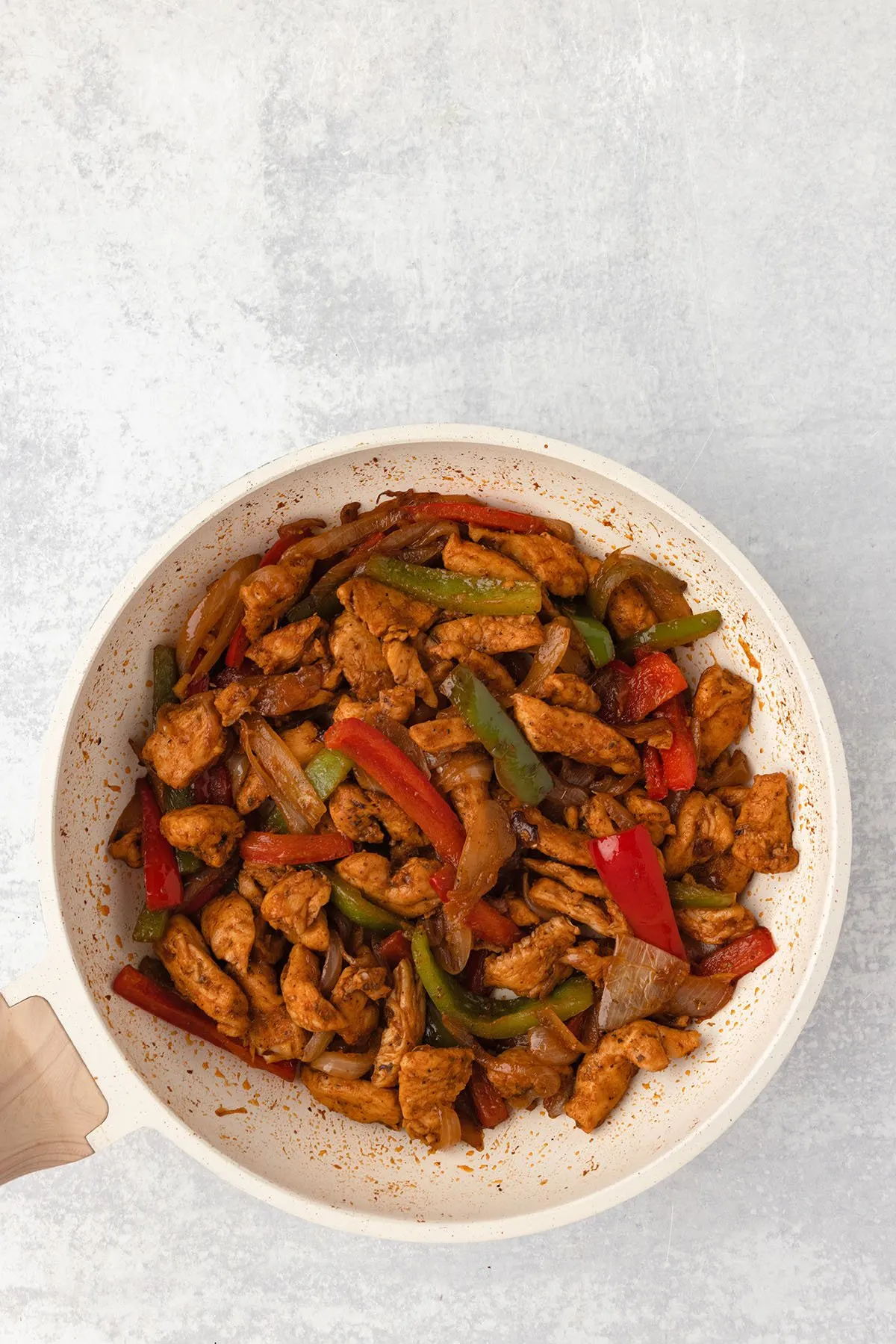 Cooked chicken, onions, red and green peppers in a skillet.