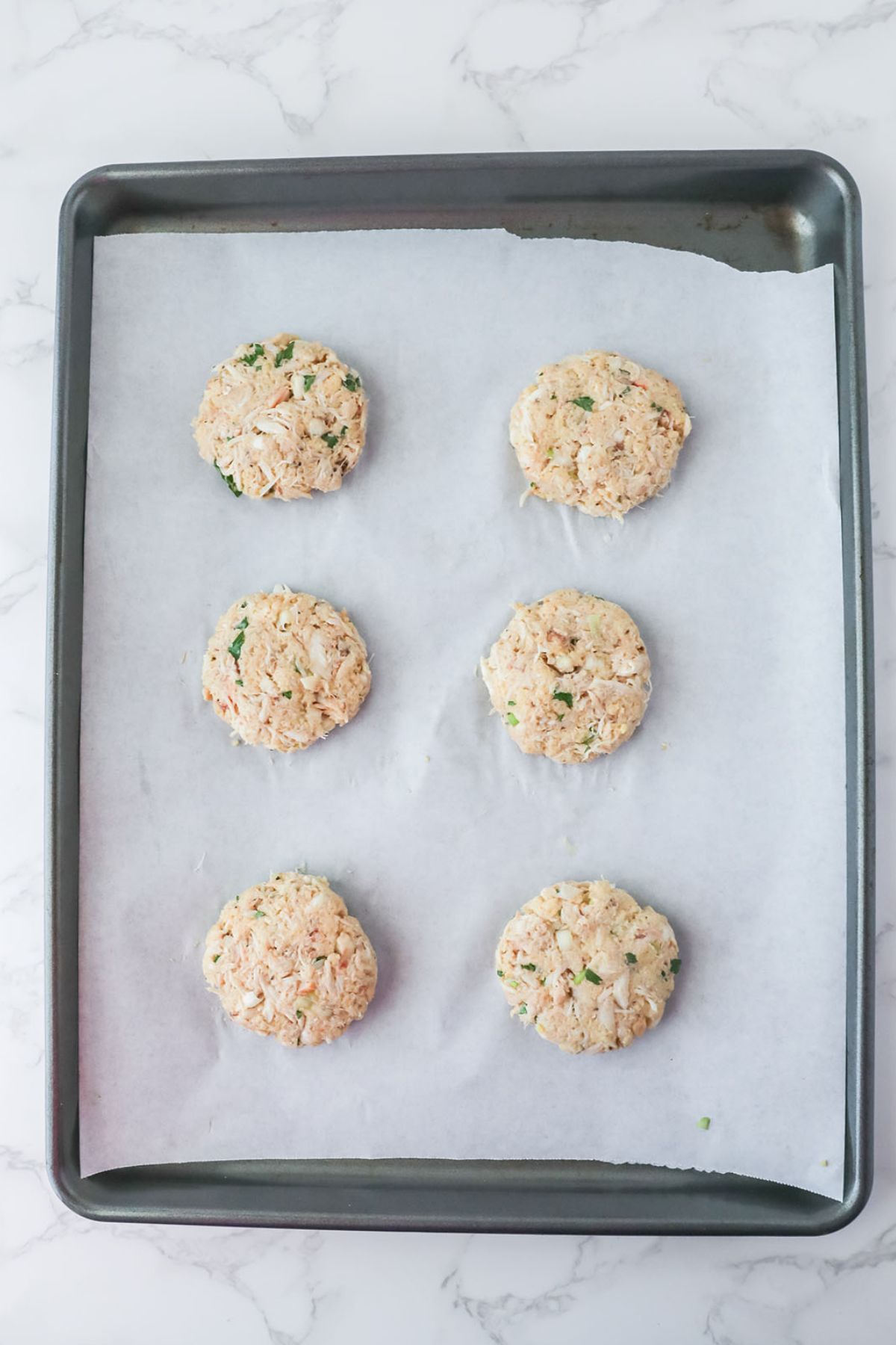 Crab cake patties are placed on a parchment paper-lined baking sheet.