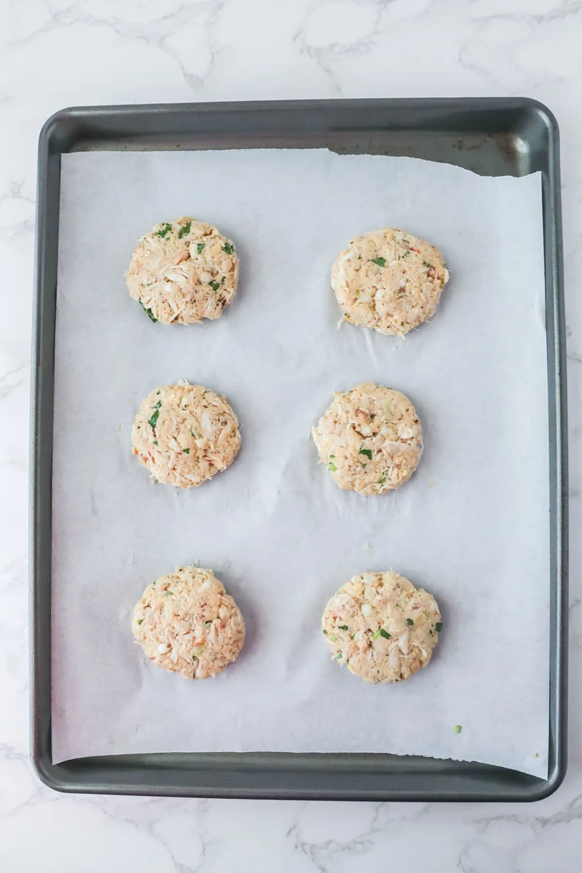 Crab cake patties are placed on a parchment paper-lined baking sheet.