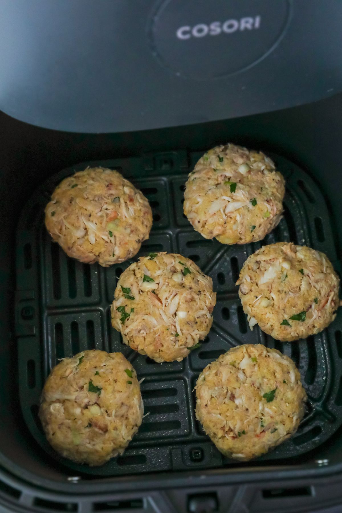 Crab cakes are placed in an air fryer basket in a single layer.