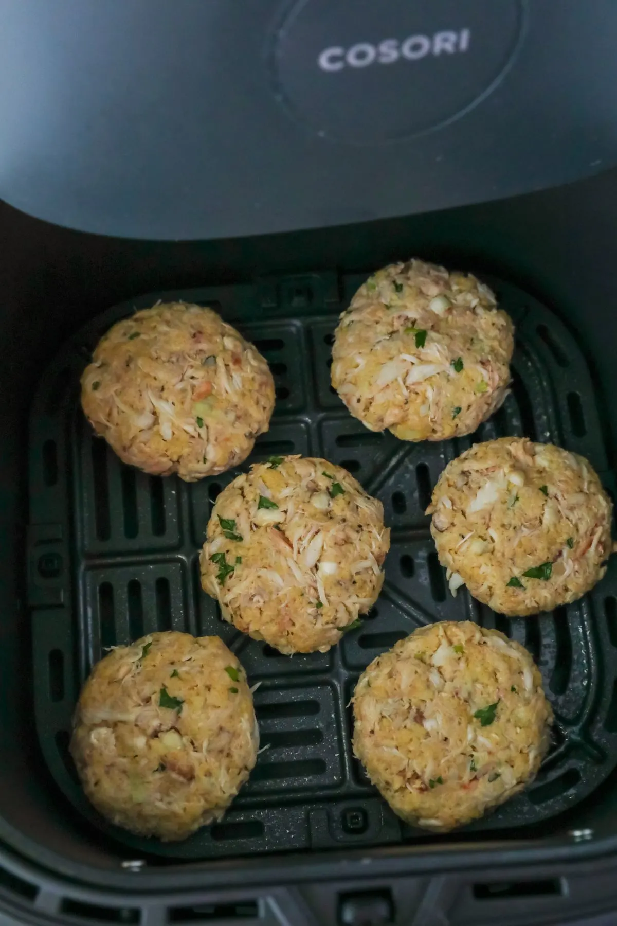 Crab cakes are placed in an air fryer basket in a single layer.