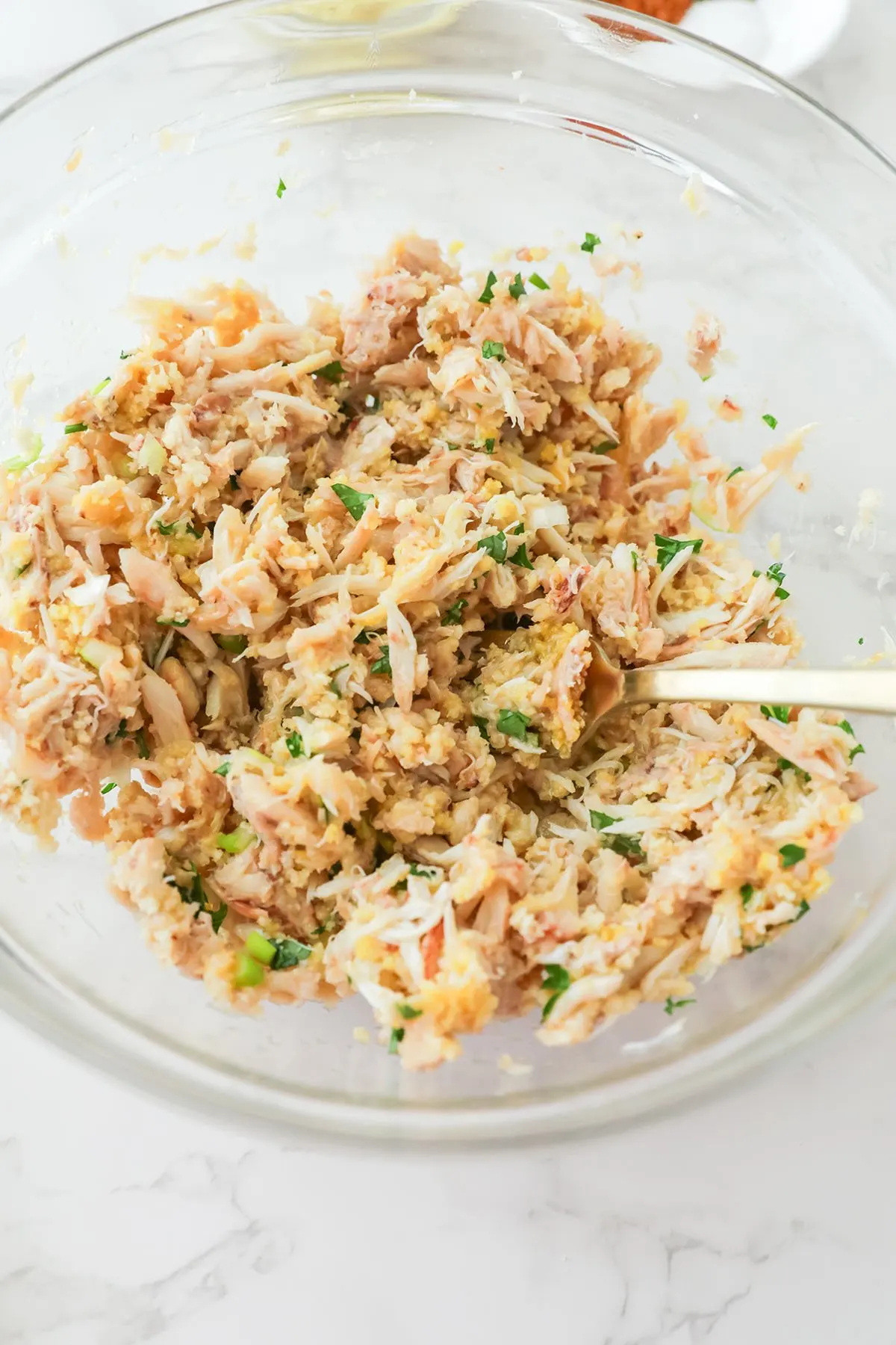Crab meat, breadcrumbs, egg, parsley, and green onion mixed together in a mixing bowl.