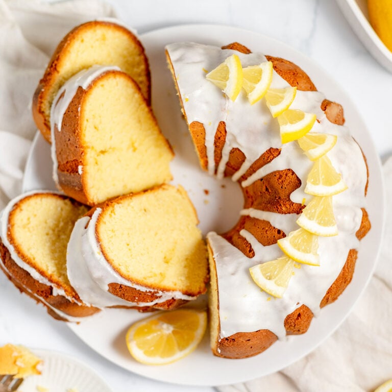 Lemon Bundt cake on a white serving plate with half the cake sliced.