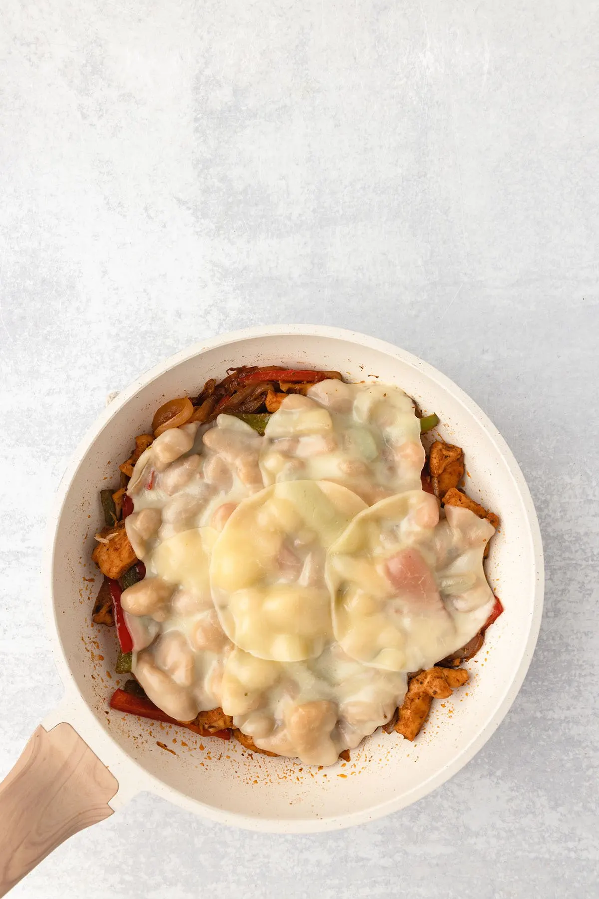 Melted Provolone cheese on top of the chicken and vegetables in the skillet.