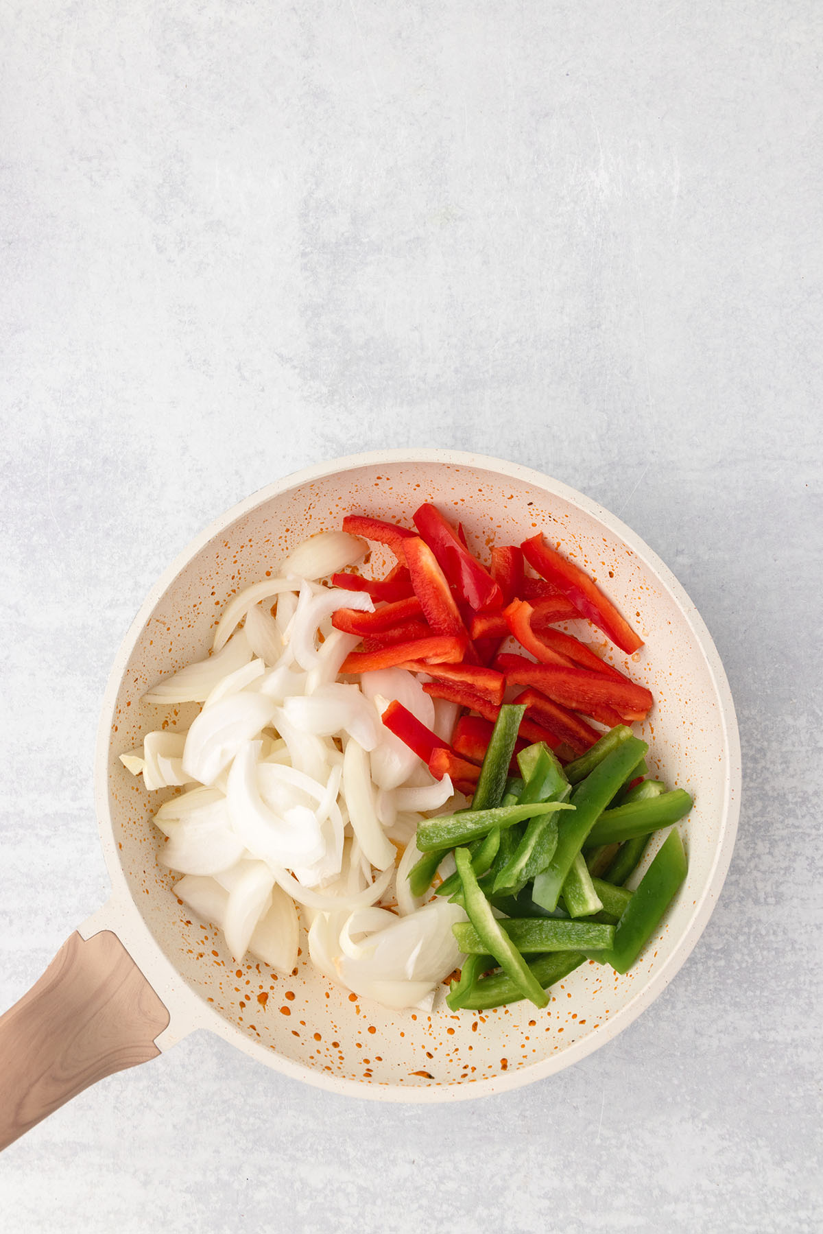 Sliced onions and red and green peppers are in a skillet.
