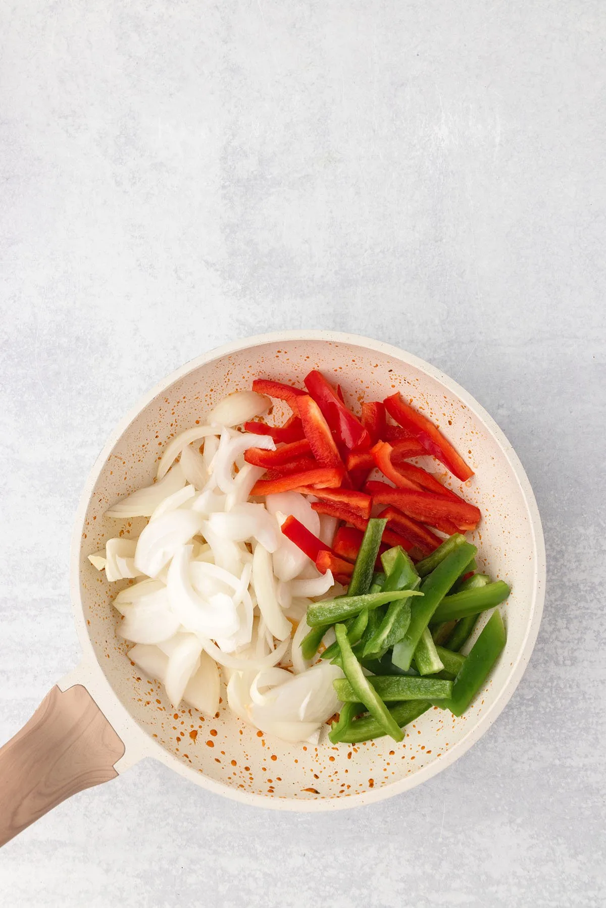 Sliced onions and red and green peppers are in a skillet.