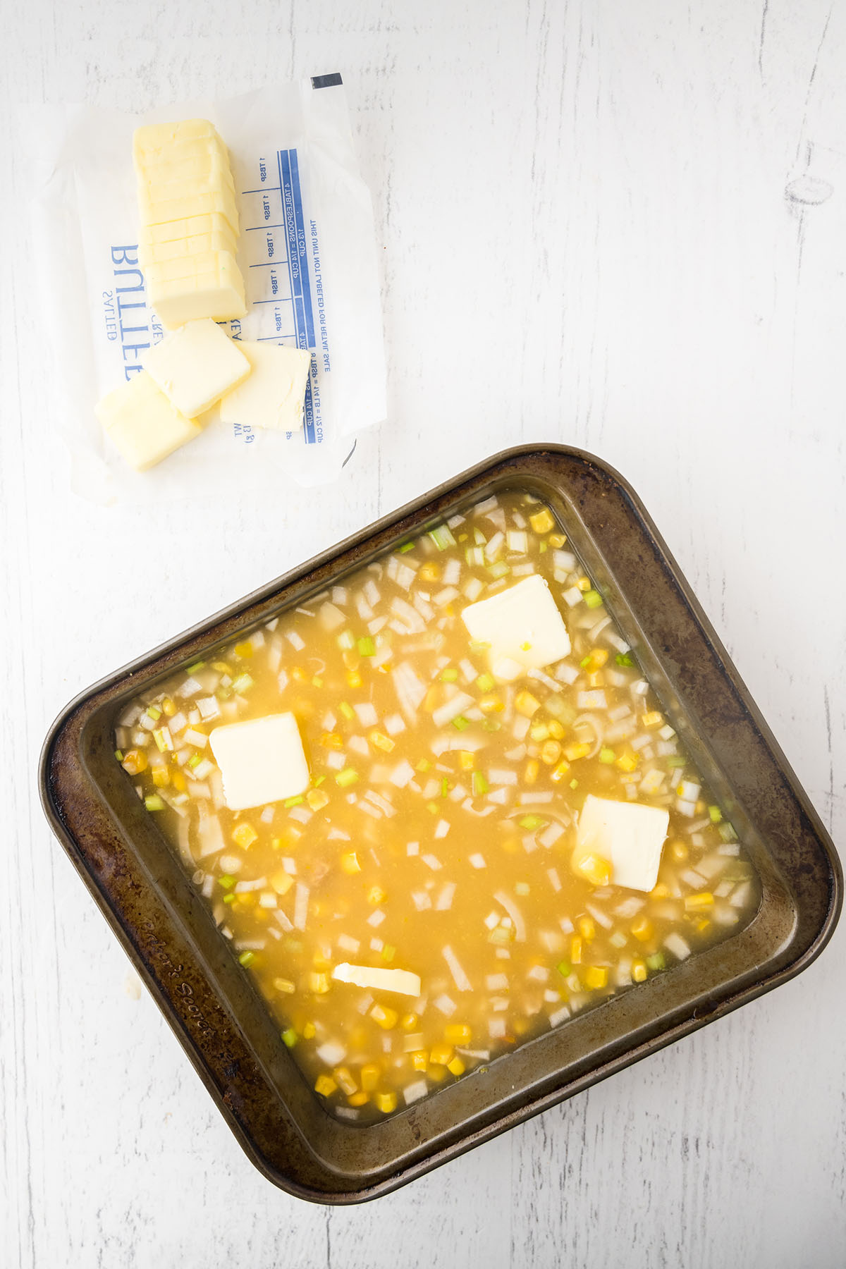 Rice, chicken broth, chicken, rice soup, onion and corn in square baking pan.
