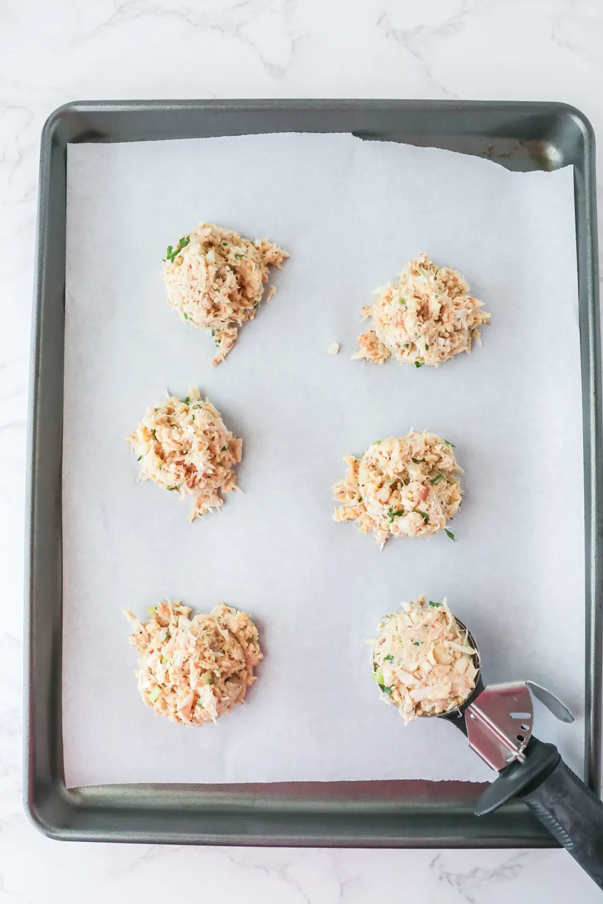 Scooped balls of crab cake mixture on a parchment paper lined baking sheet.