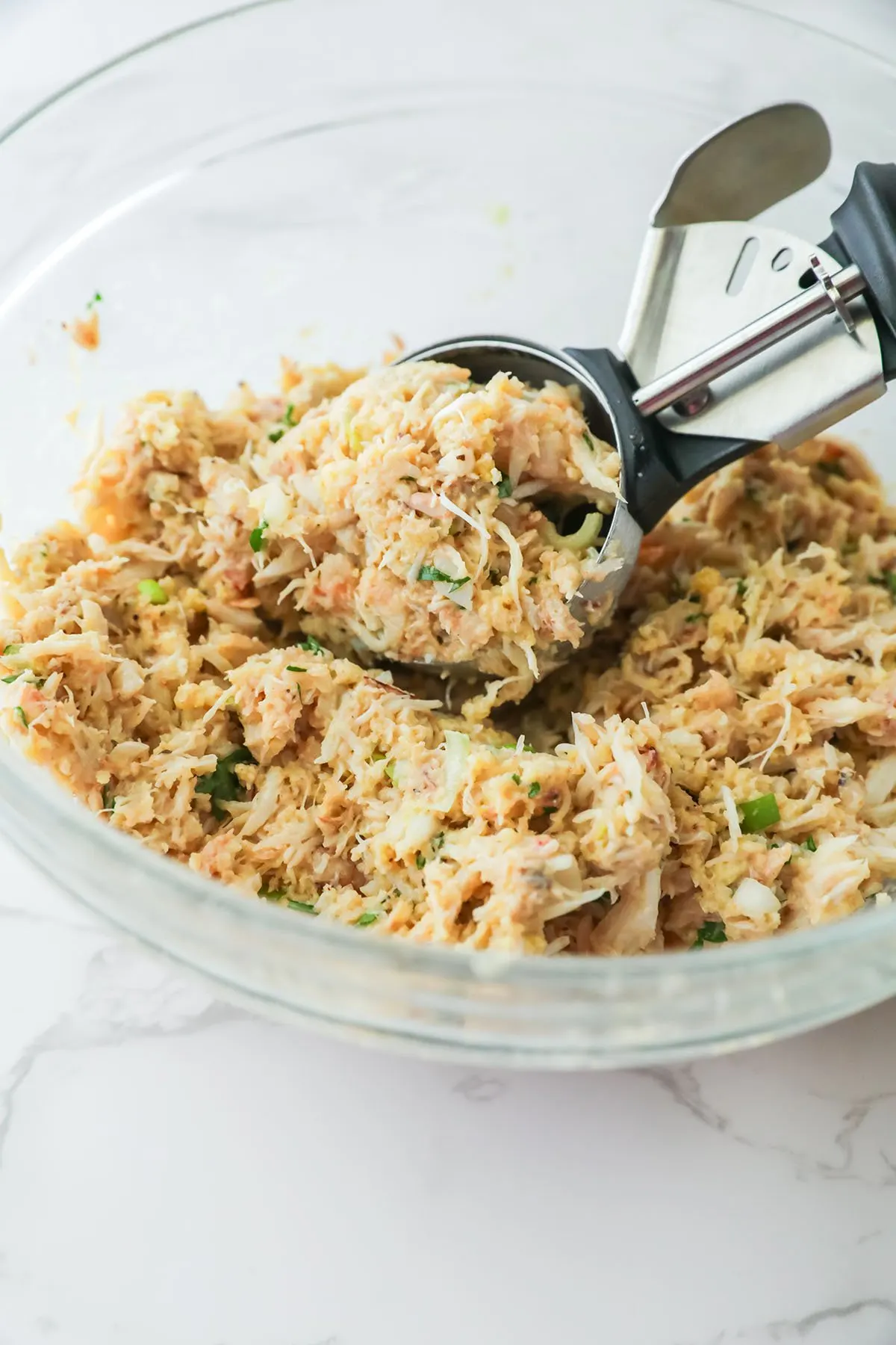 Scooping crab cake mixture from the mixing bowl with a large cookie scoop.