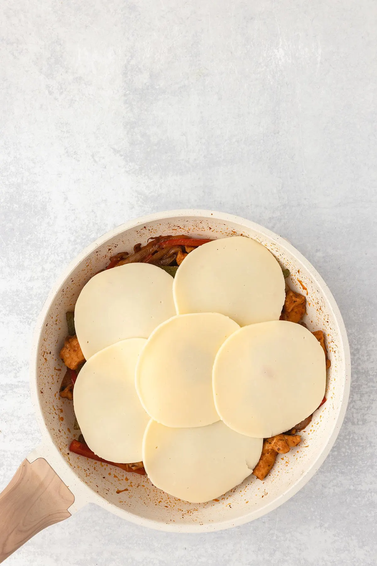 Sliced Provolone cheese is placed on top of the chicken and vegetables in the skillet.