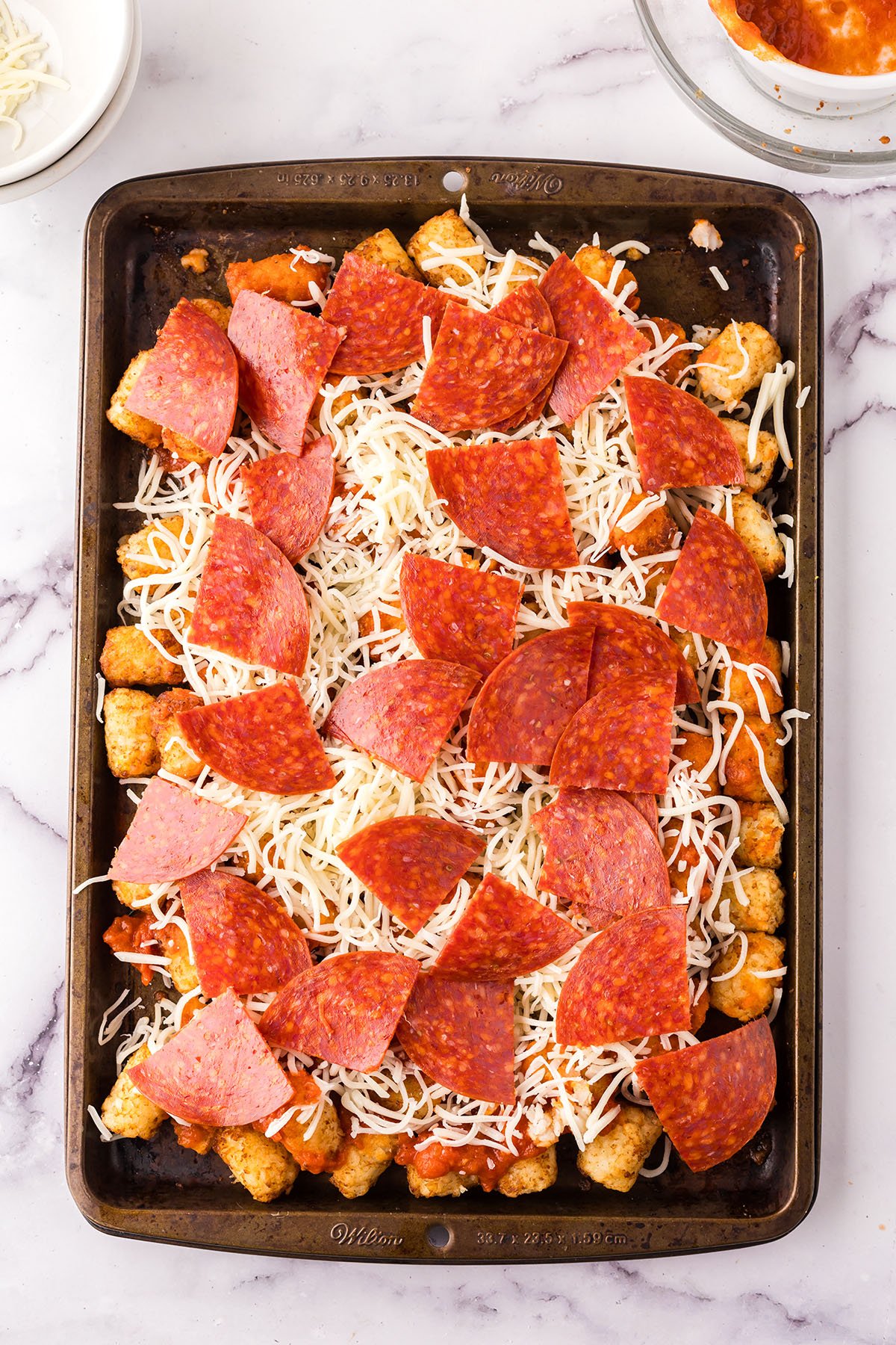 Tater tots tossed with marinara sauce, cheese and pepperoni on a baking sheet.