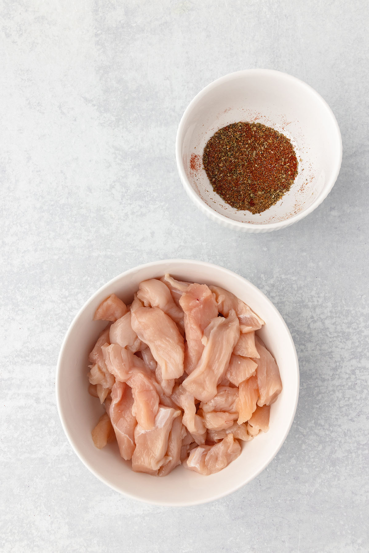 Thinly sliced chicken in a large bowl and seasonings in a small bowl.