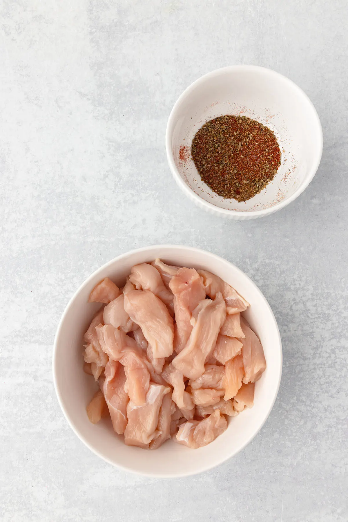 Thinly sliced chicken in a large bowl and seasonings in a small bowl.