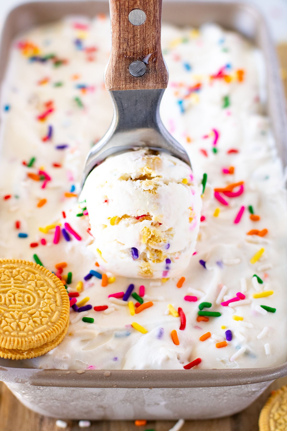 A scoop of Funfetti Golden Oreo Ice Cream being served out of the frozen ice cream in a metal loaf pan. 