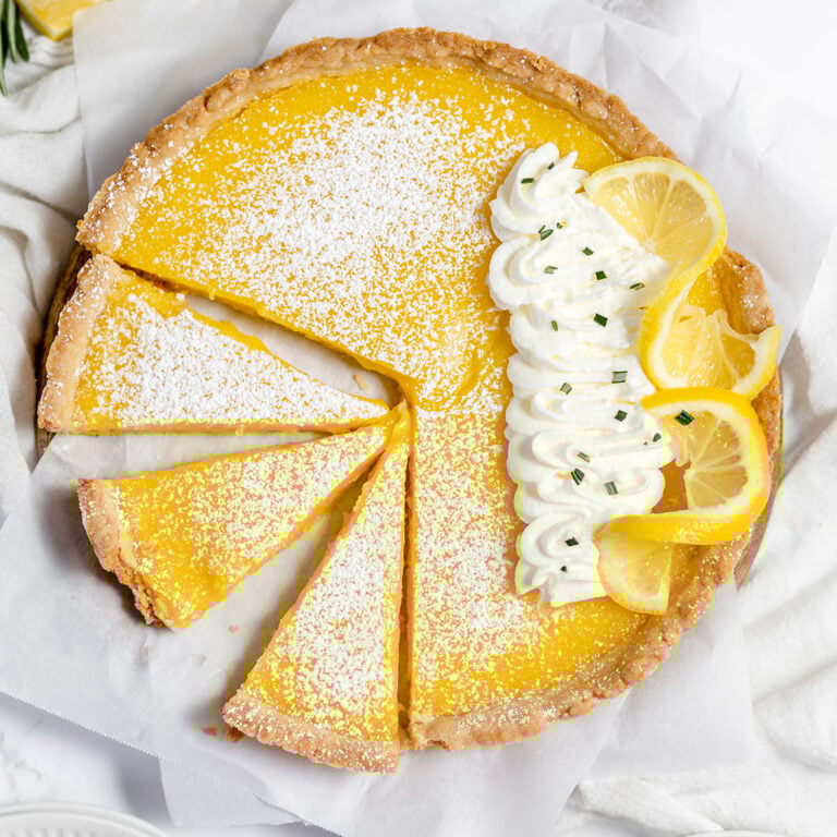 Lemon Tart topped with whipped cream with three slices cut and ready to serve.