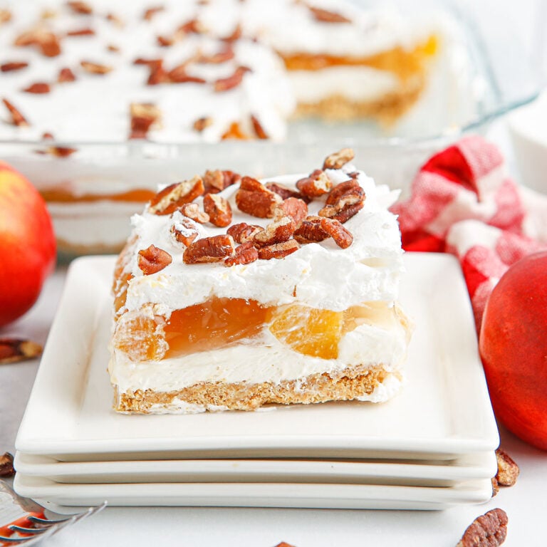 A slice of peach delight topped with chopped peans on a white plate.