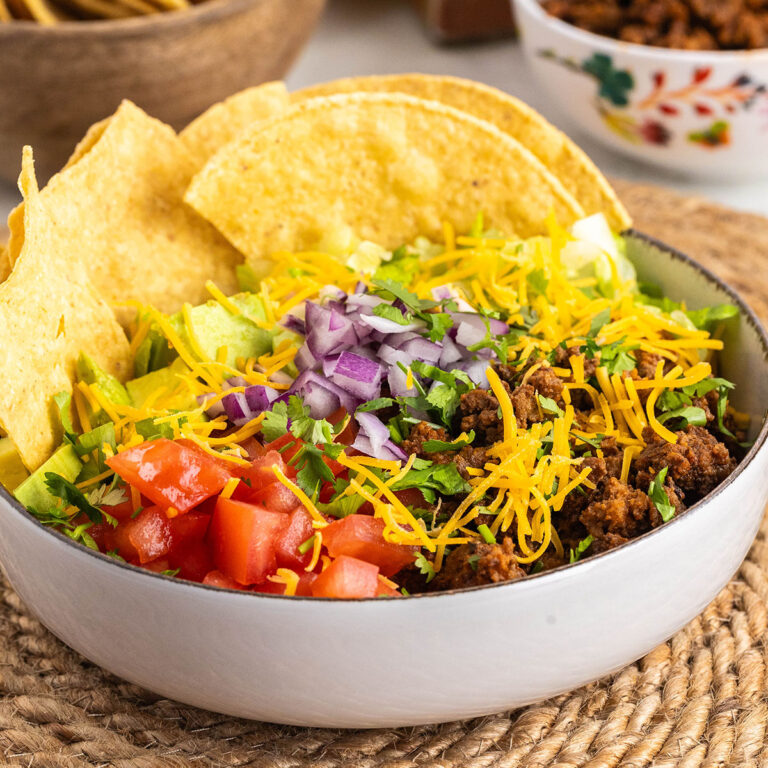 Beef taco salad in a white bowl with tortilla chips.