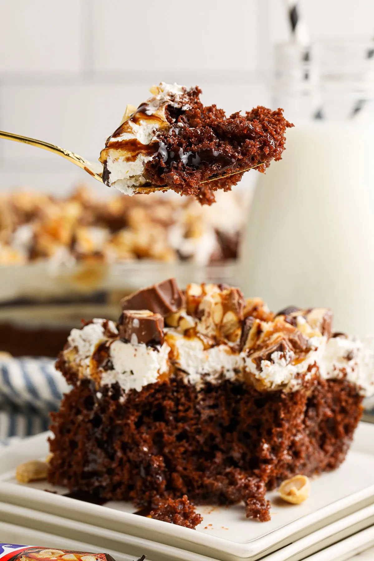 Chocolate Snickers Poke Cake on white plate with a bite on a fork.