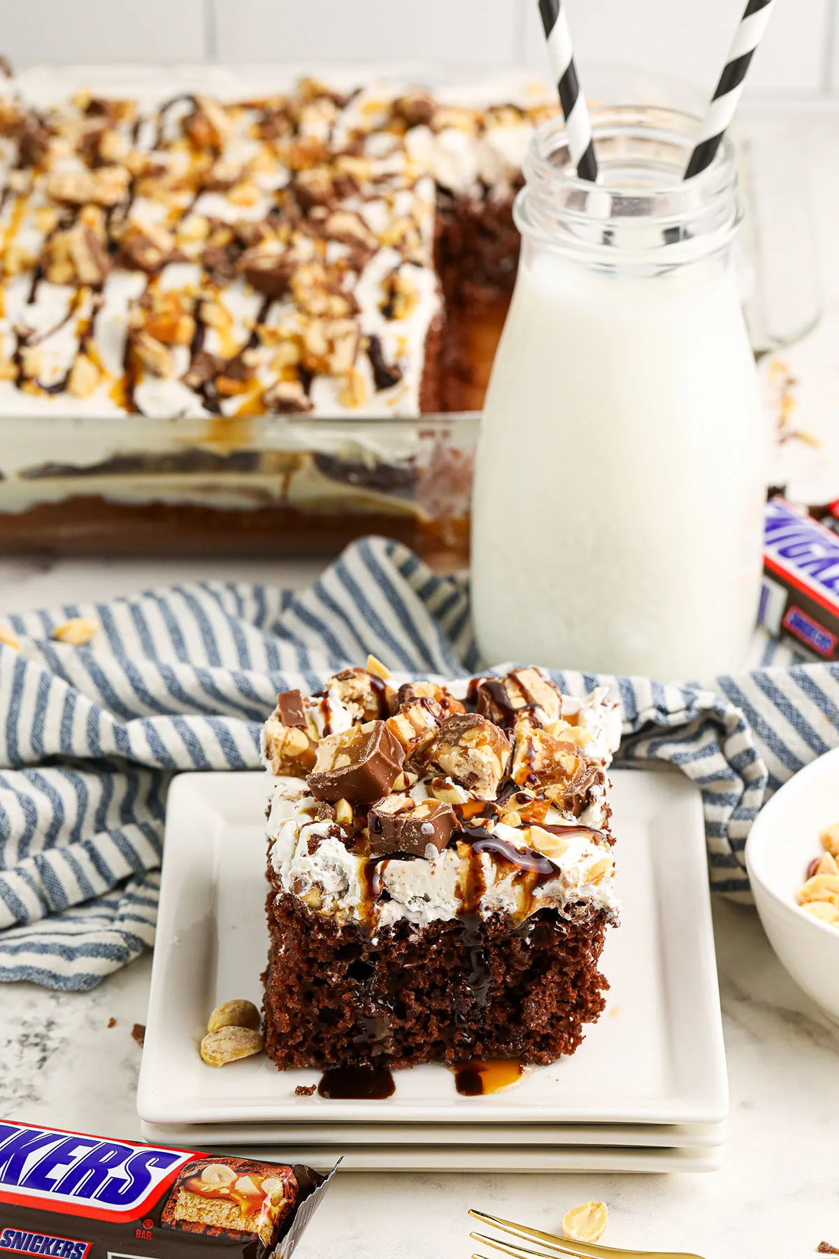 A slice of Snickers Poke Cake on a white square plate.