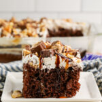 A slice of Snickers Poke Cake on a white plate.