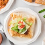Taco Pocket topped with shredded lettuce, sour cream, and salsa on a white plate.