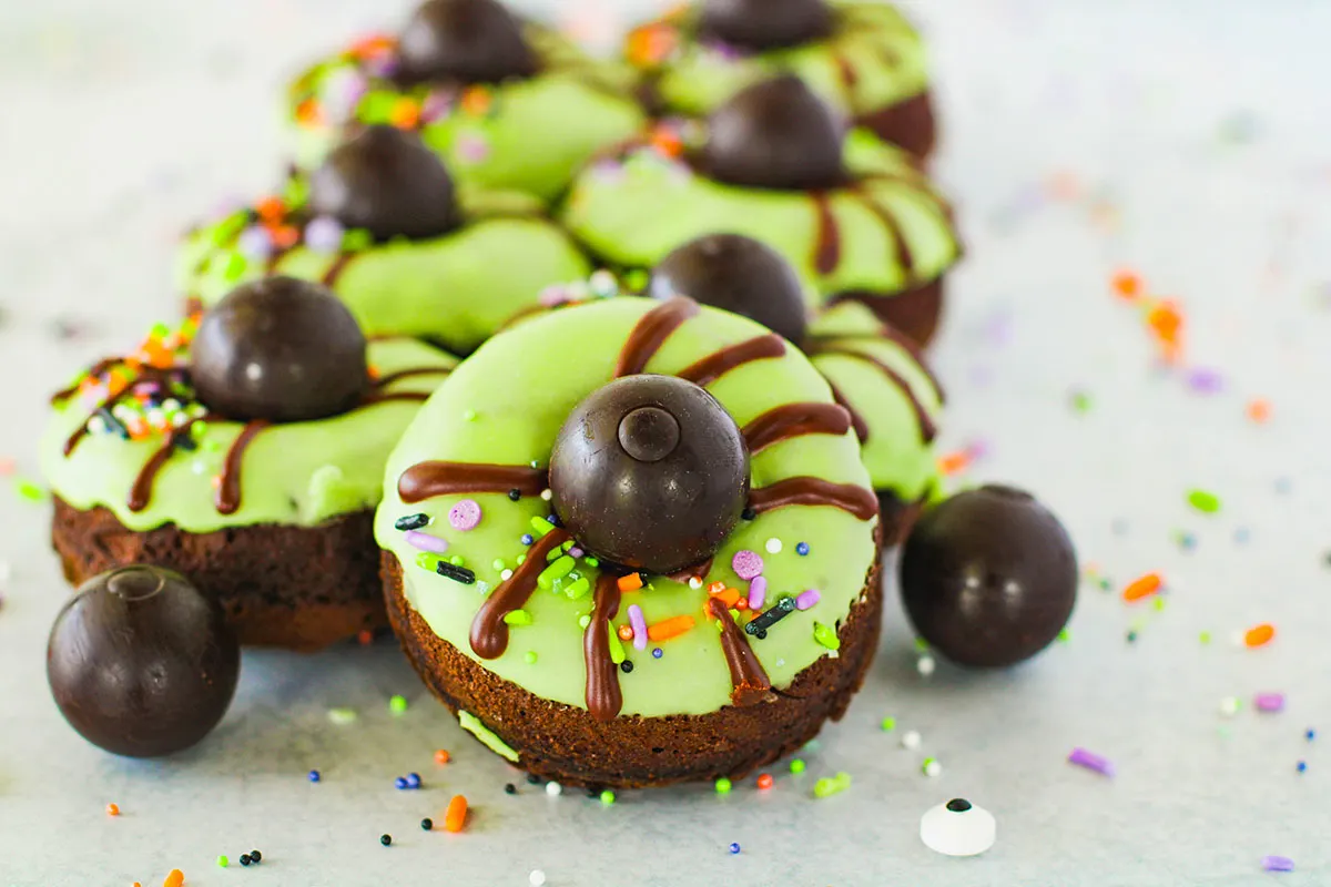 Chocolate Spider Donuts with green glaze and sprinkles on the counter top.