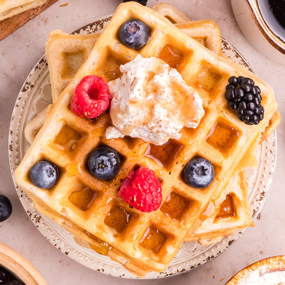 Homemade waffles on a plate topped with cinnamon whipped cream and berries.